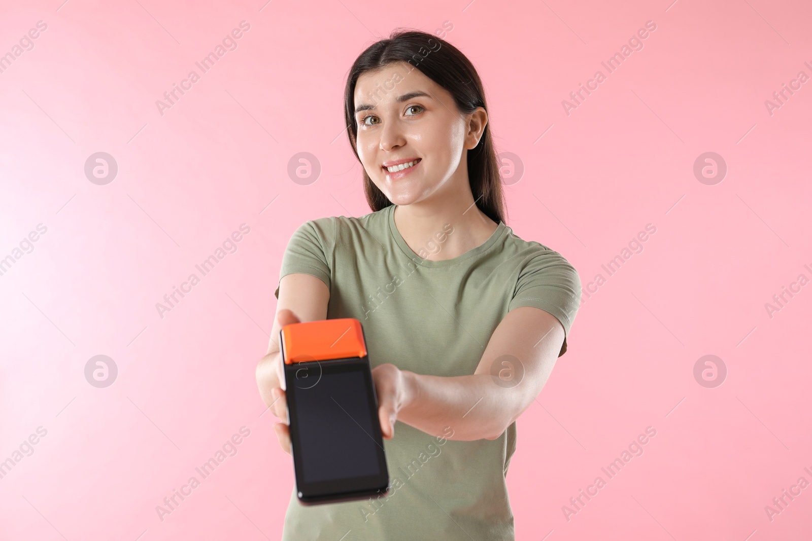 Photo of Happy young woman with payment terminal on pink background