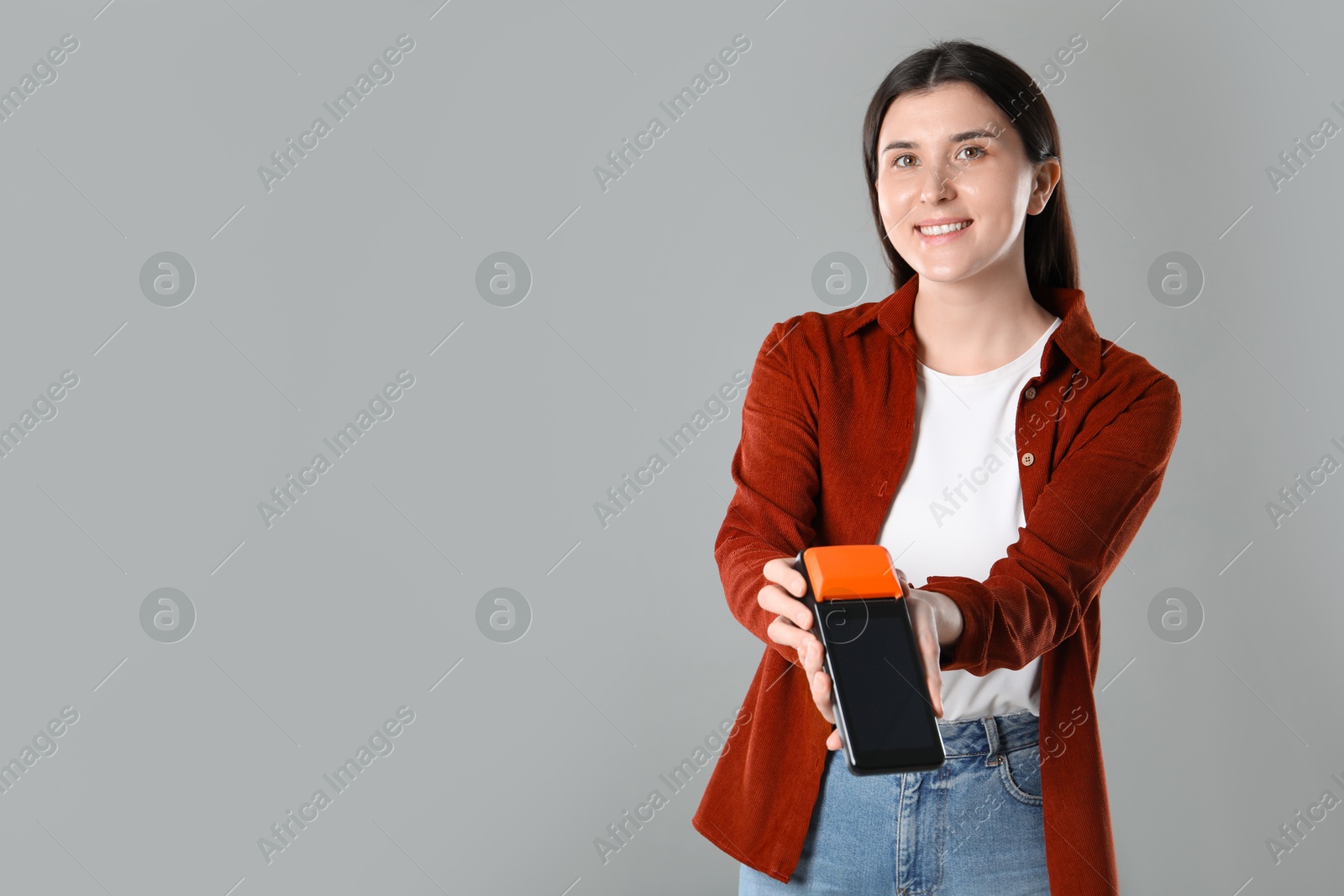 Photo of Happy young woman with payment terminal on gray background, space for text