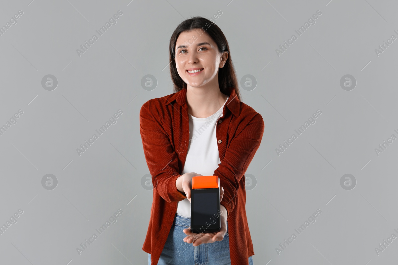 Photo of Happy young woman with payment terminal on gray background