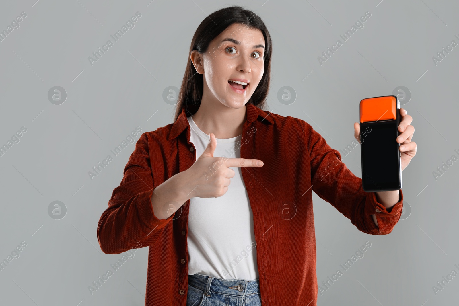 Photo of Emotional young woman with payment terminal on gray background