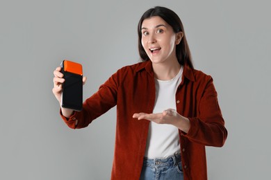 Photo of Emotional young woman with payment terminal on gray background