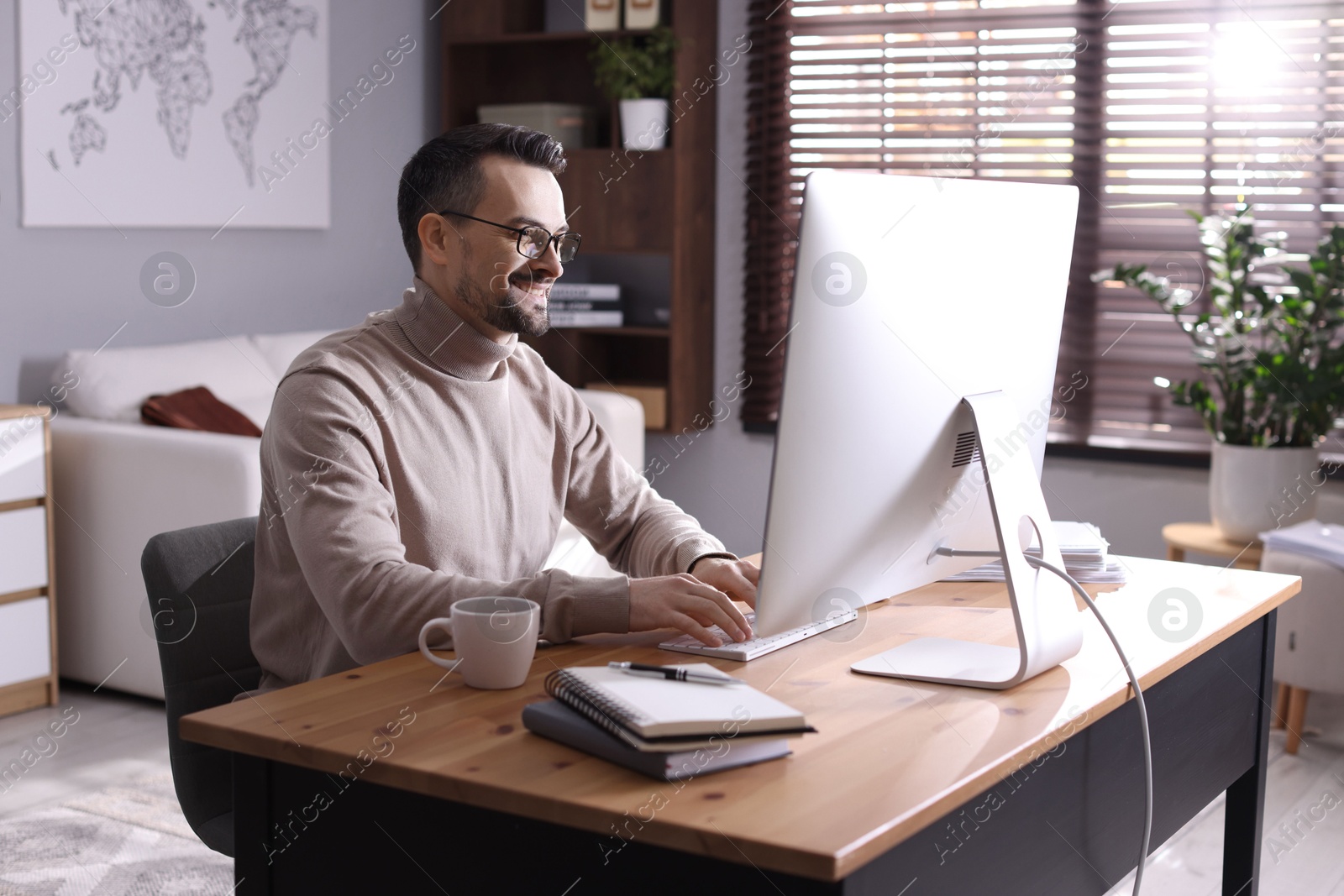 Photo of Happy man working with computer at desk indoors. Home office