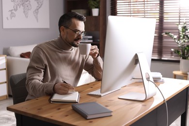 Photo of Handsome man working with computer at desk indoors. Home office