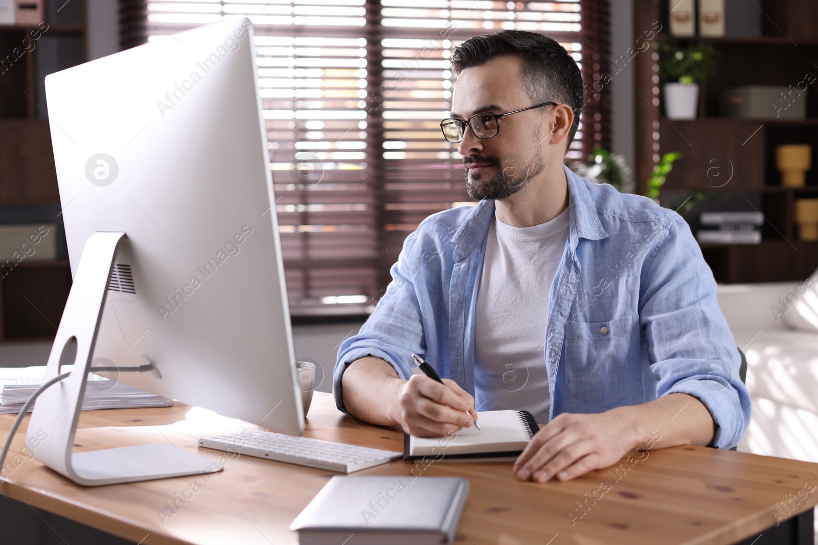 Photo of Handsome man working with computer at desk indoors. Home office