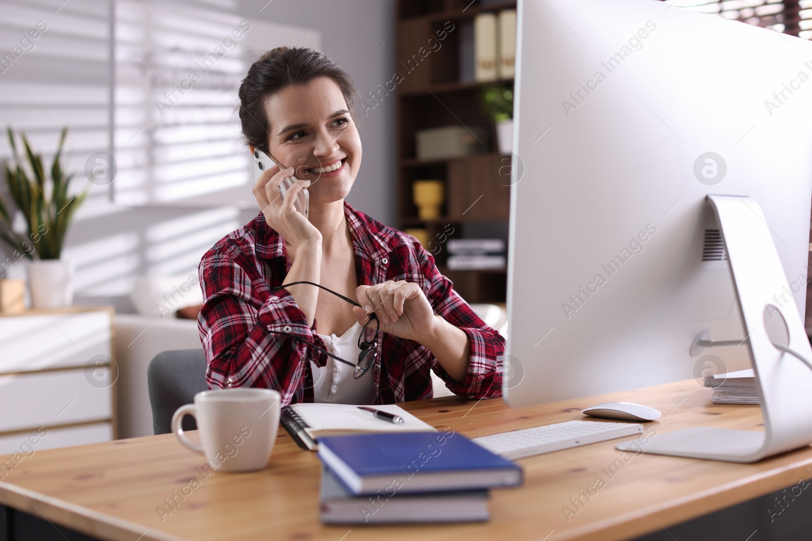 Photo of Happy woman talking by smartphone at desk with computer indoors. Home office