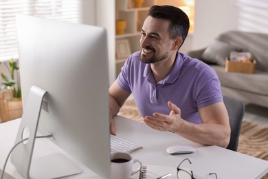 Photo of Happy man having videochat by computer at desk indoors. Home office