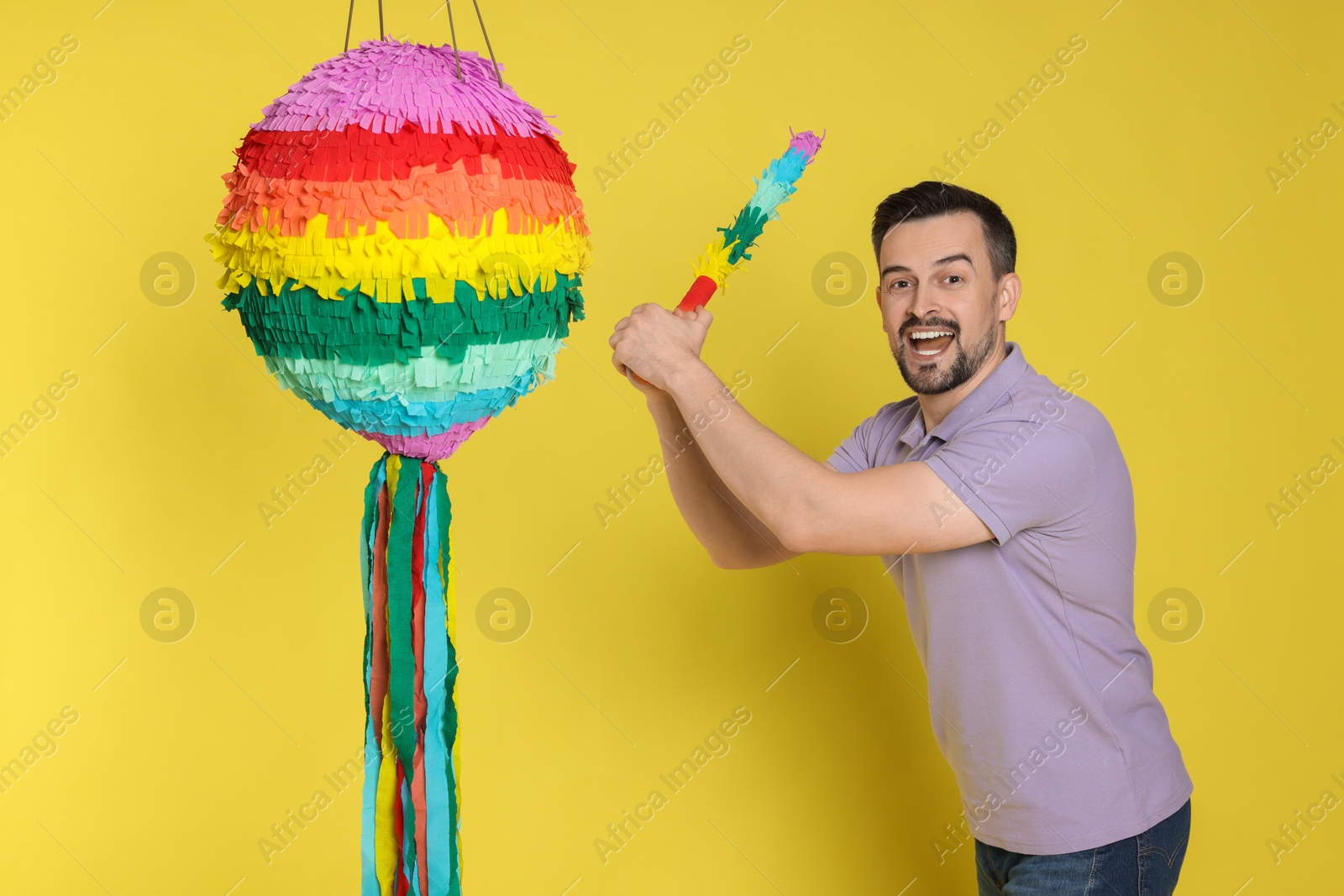 Photo of Emotional man hitting colorful pinata with stick on yellow background