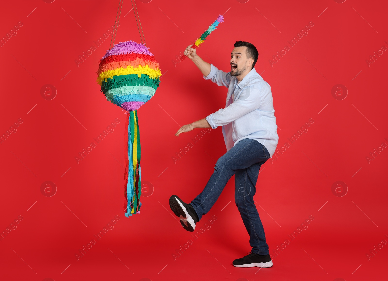 Photo of Happy man hitting colorful pinata with stick on red background