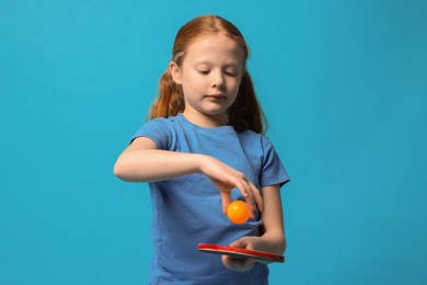 Photo of Little girl with ping pong racket and ball on light blue background