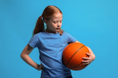 Photo of Little girl with basketball ball on light blue background