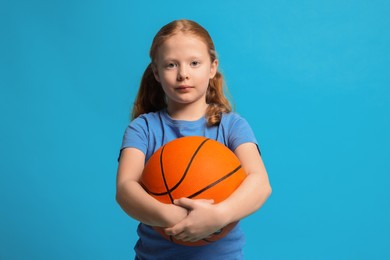 Photo of Little girl with basketball ball on light blue background