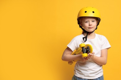 Photo of Little girl in helmet with penny board on orange background, space for text