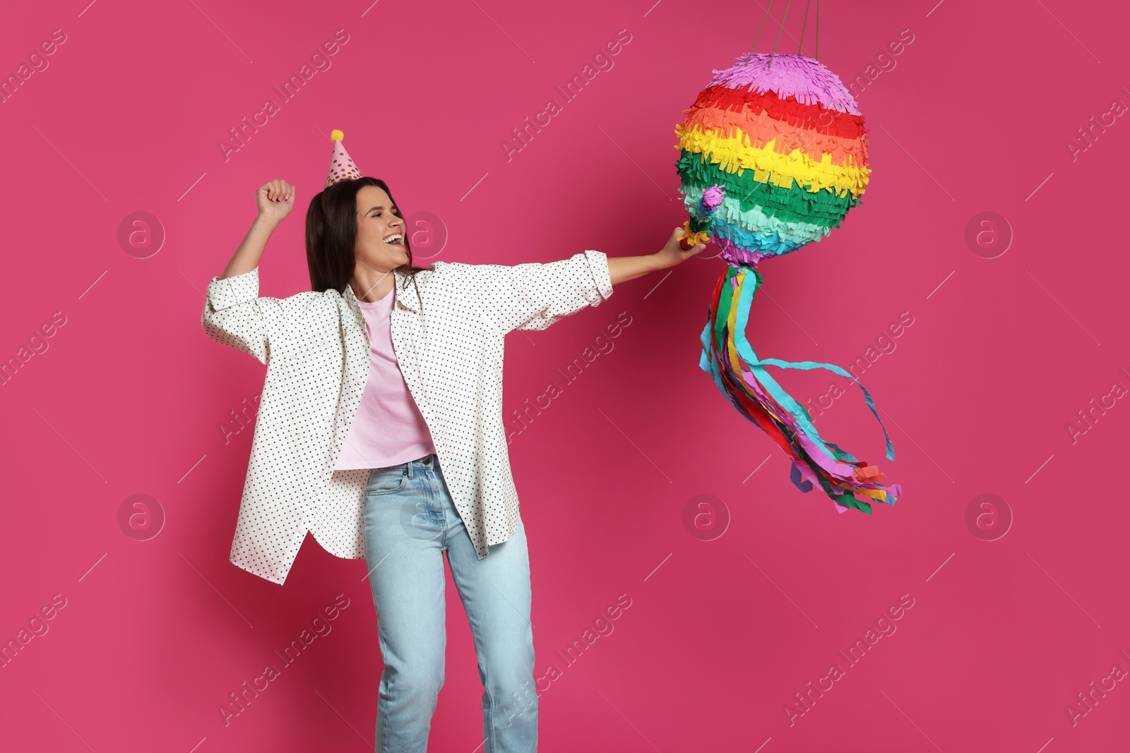 Photo of Happy woman hitting colorful pinata with stick on pink background