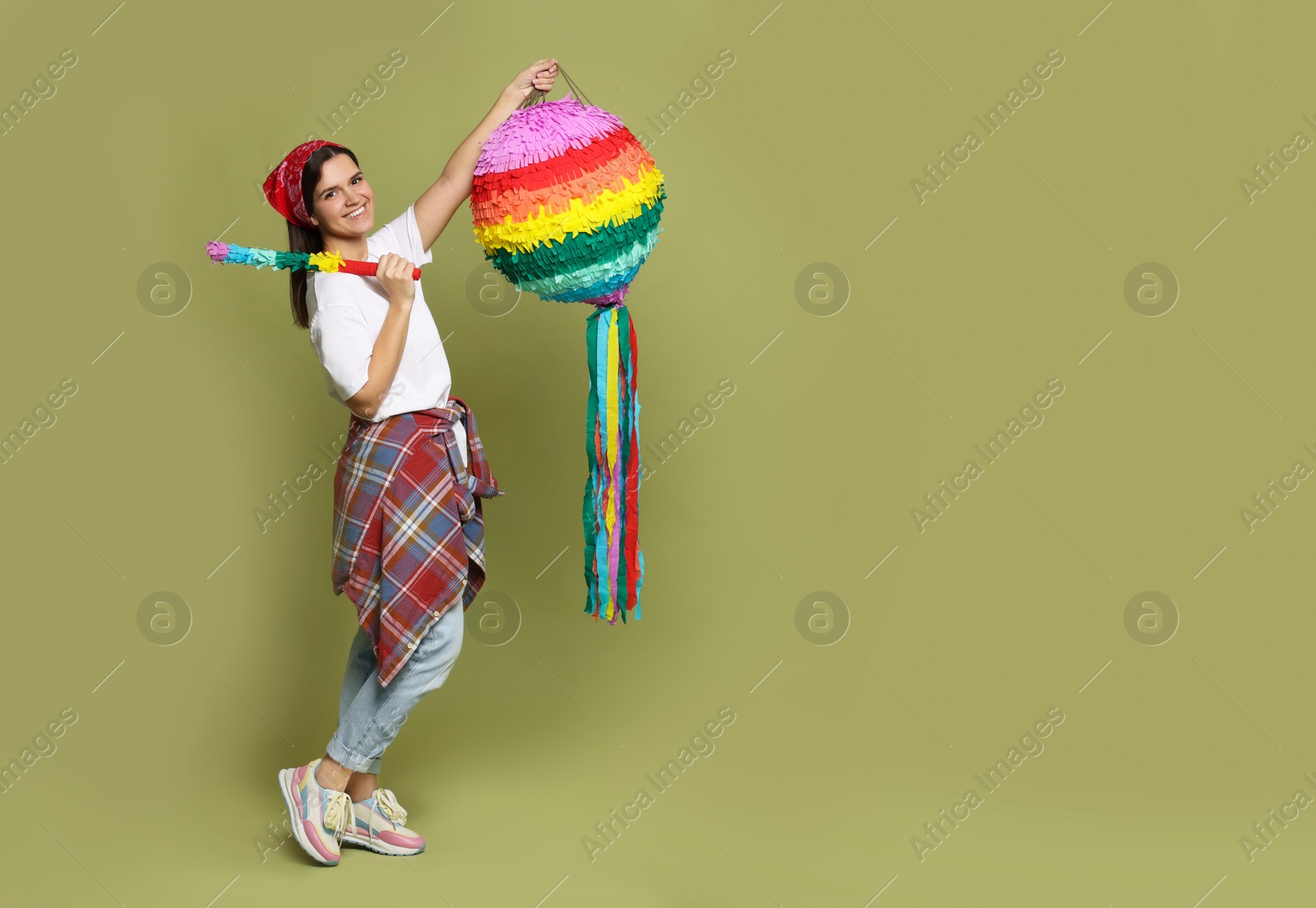 Photo of Happy woman with colorful pinata and stick on green background, space for text