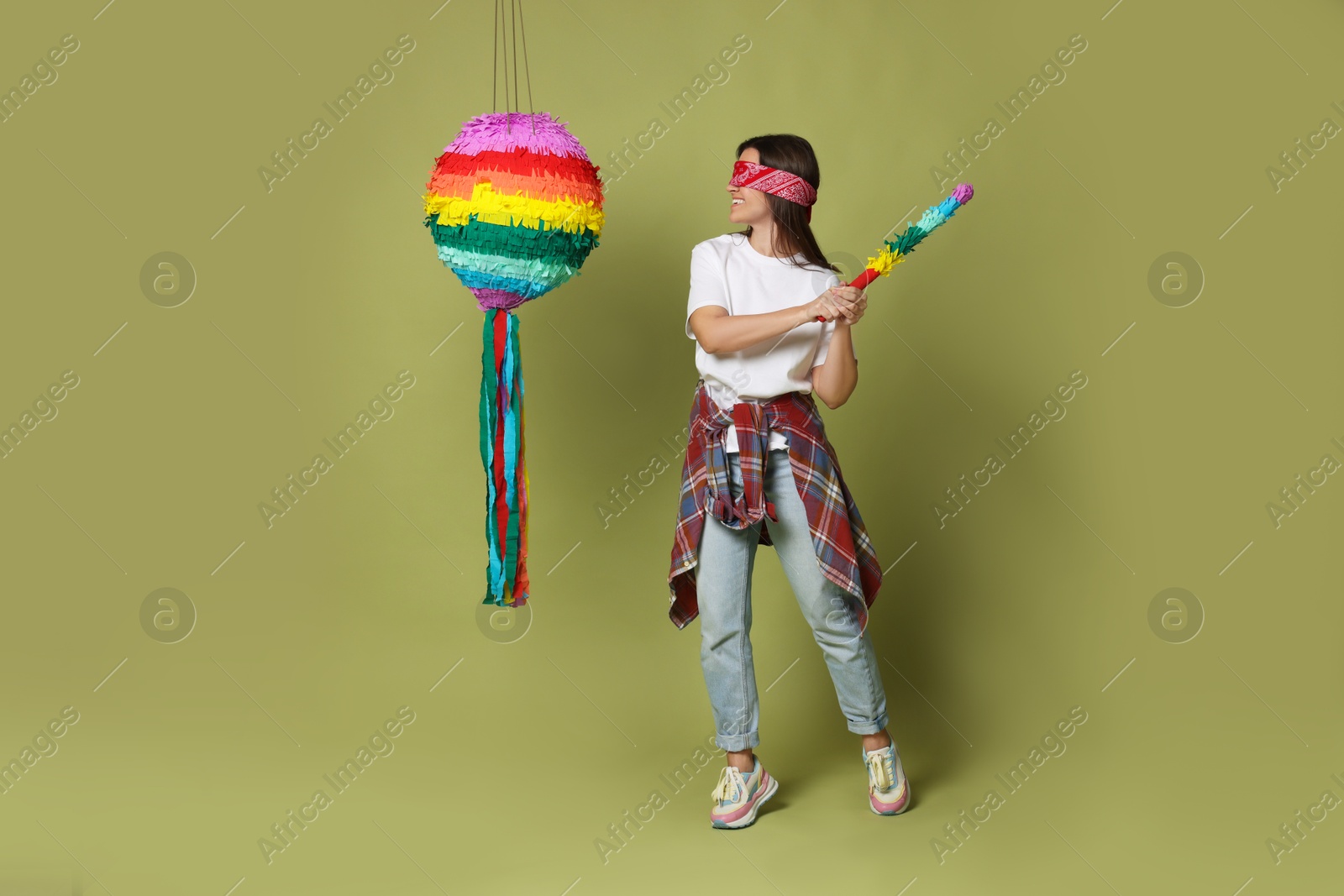 Photo of Woman with tied eyes breaking pinata on green background