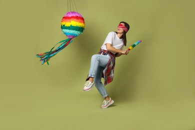 Photo of Woman with tied eyes breaking pinata on green background