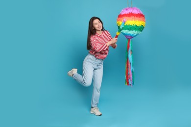 Happy woman hitting colorful pinata with stick on light blue background