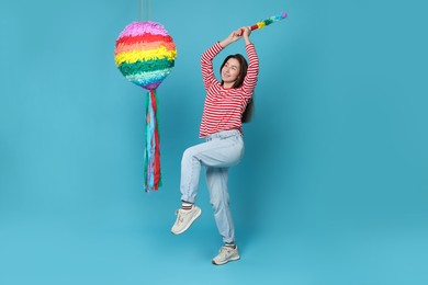 Photo of Happy woman hitting colorful pinata with stick on light blue background