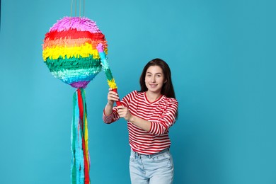 Happy woman with colorful pinata and stick on light blue background