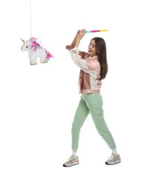 Photo of Happy woman breaking unicorn shaped pinata with stick isolated on white