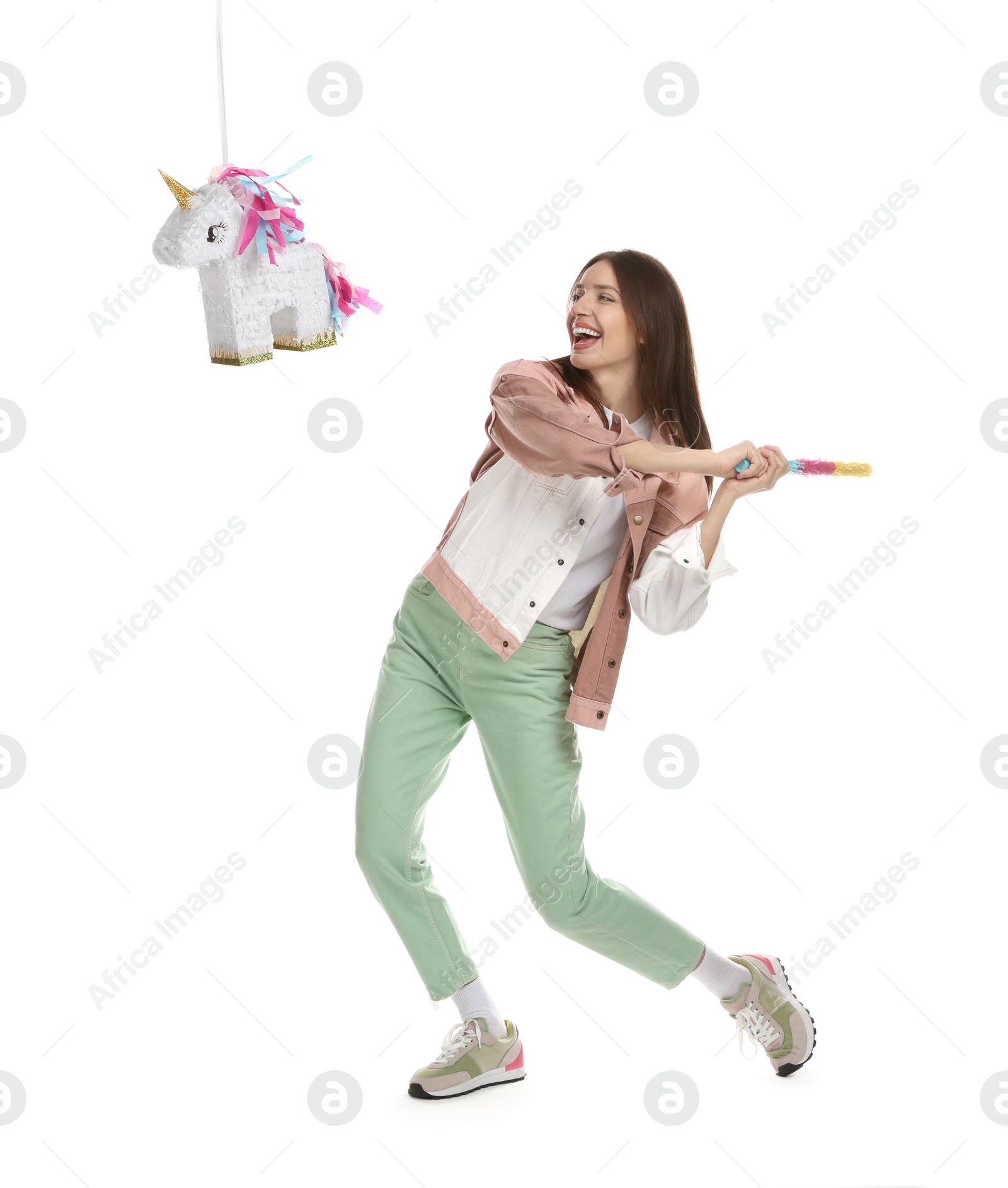 Photo of Happy woman breaking unicorn shaped pinata with stick isolated on white