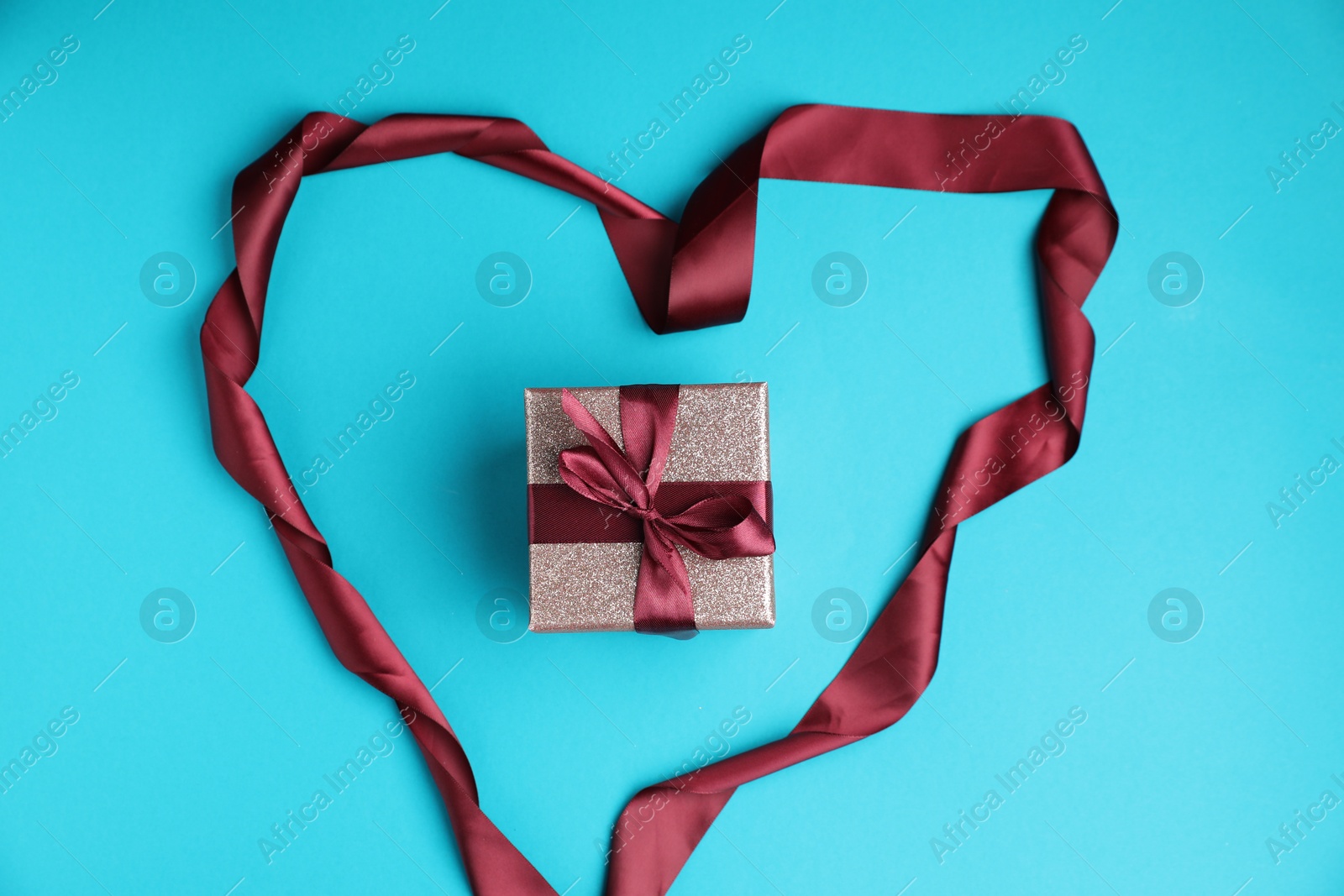 Photo of Romantic gift and heart made of ribbon on light blue background, top view