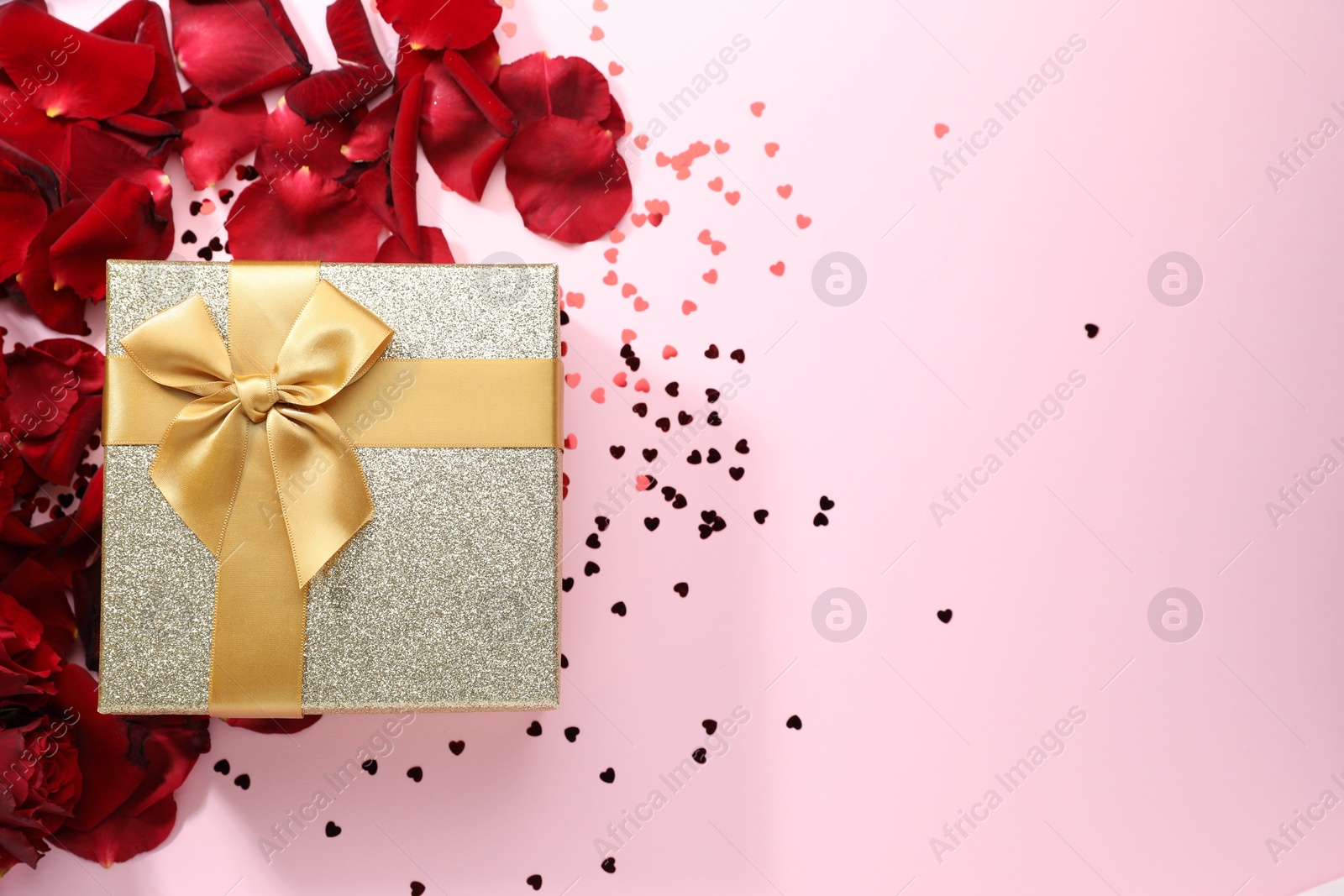 Photo of Romantic gift, rose petals and confetti on light pink background, flat lay