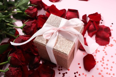 Photo of Romantic gift, roses and confetti on light pink background, closeup