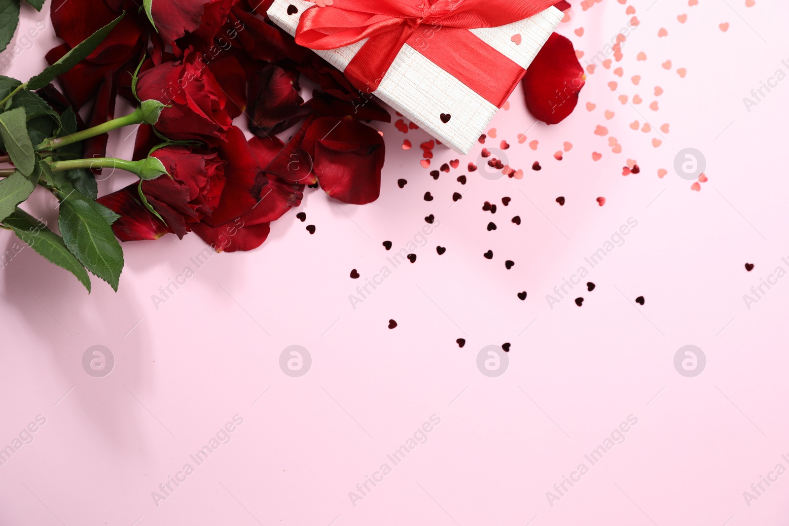 Photo of Romantic gift, roses and confetti on light pink background, flat lay. Space for text