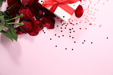 Photo of Romantic gift, roses and confetti on light pink background, flat lay. Space for text