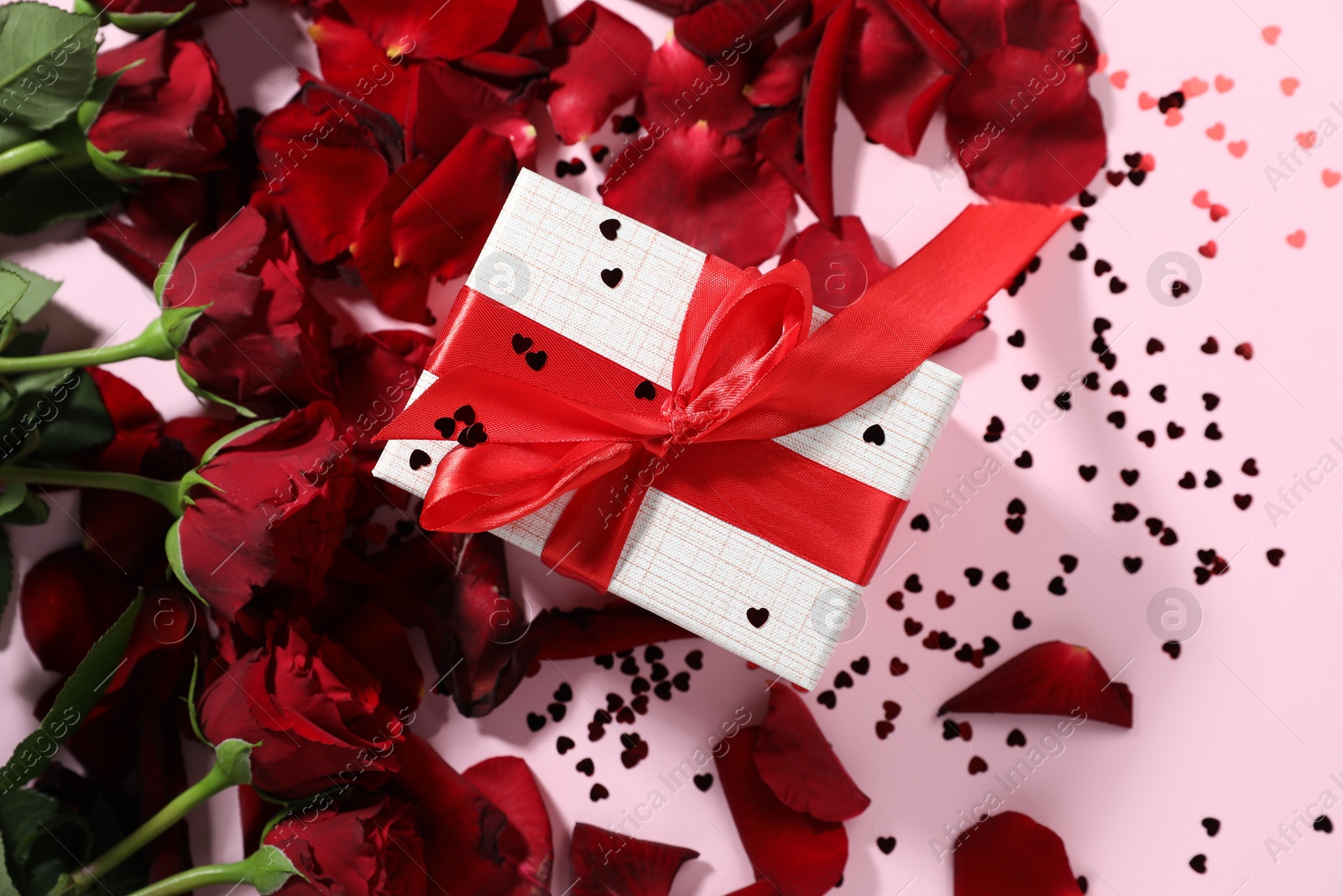 Photo of Romantic gift, roses and confetti on light pink background, flat lay