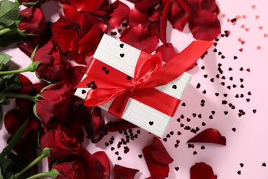 Photo of Romantic gift, roses and confetti on light pink background, flat lay