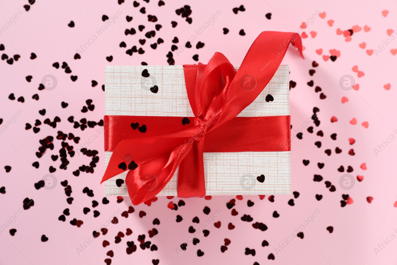 Photo of Romantic gift and confetti on light pink background, top view