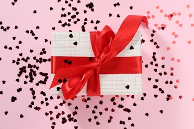 Romantic gift and confetti on light pink background, top view