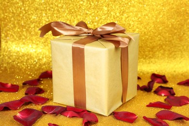 Photo of Romantic gift and rose petals on golden background, closeup