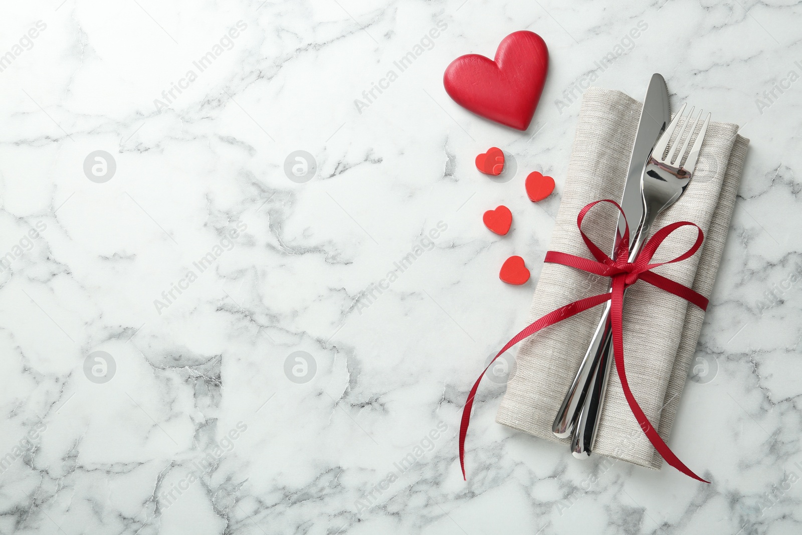 Photo of Romantic place setting for Valentine's day. Cutlery with napkin and red decorative hearts on white marble table, top view. Space for text