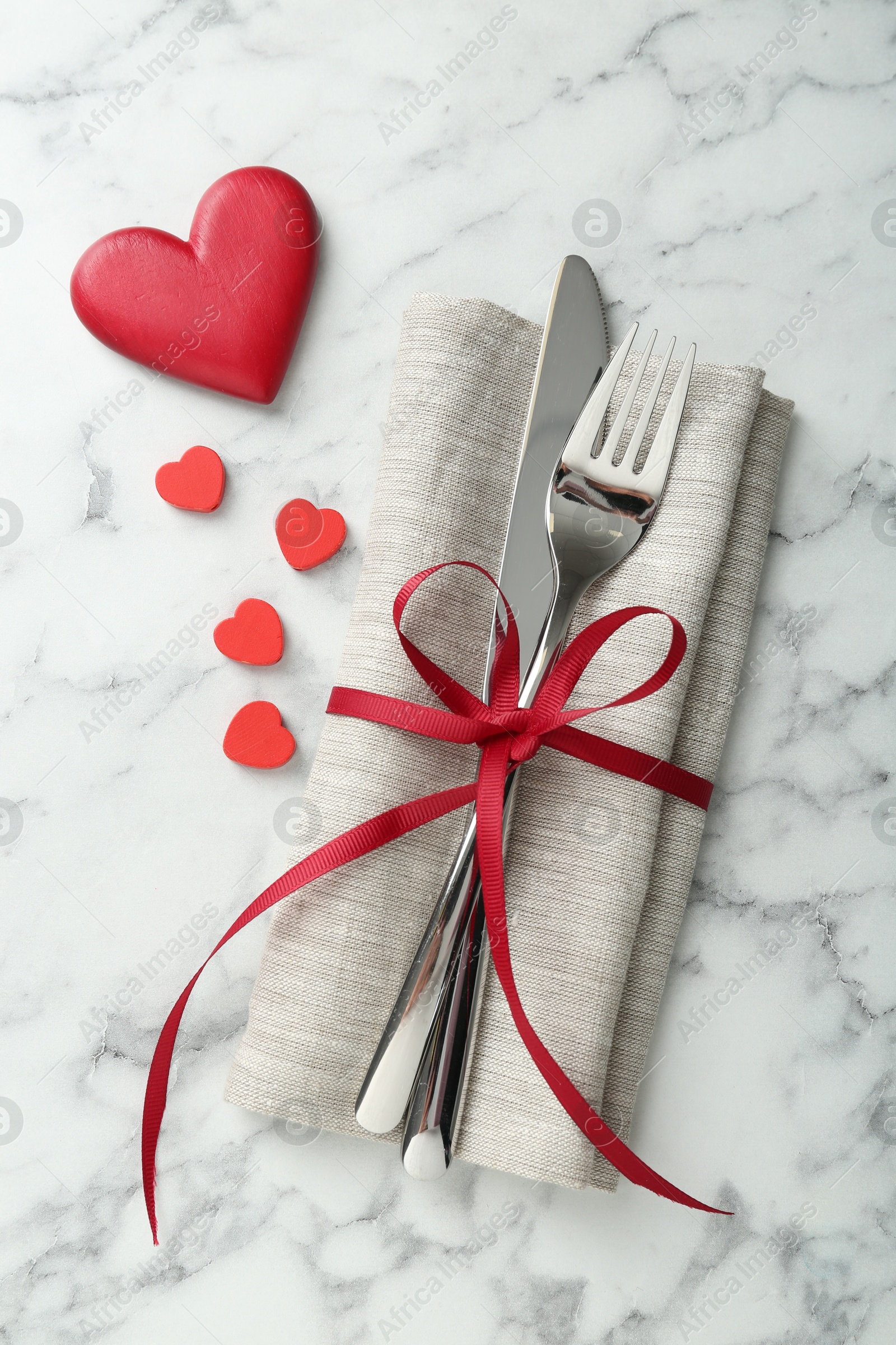 Photo of Romantic place setting for Valentine's day. Cutlery with napkin and red decorative hearts on white marble table, top view