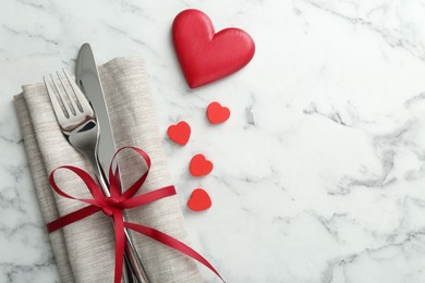 Photo of Romantic place setting for Valentine's day. Cutlery with napkin and red decorative hearts on white marble table, top view. Space for text