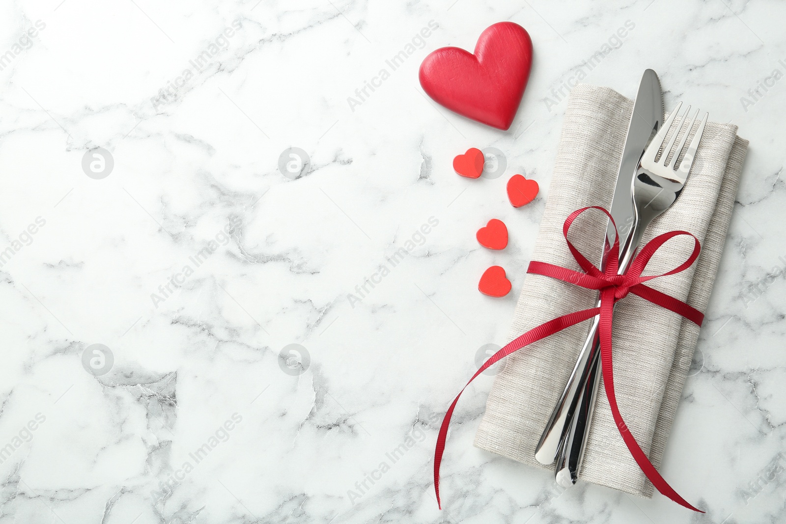 Photo of Romantic place setting for Valentine's day. Cutlery with napkin and red decorative hearts on white marble table, top view. Space for text