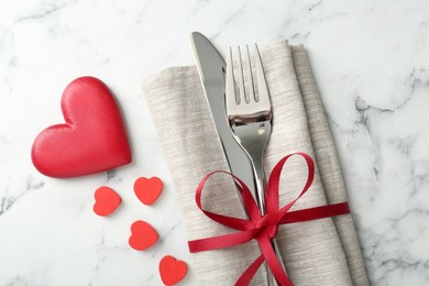 Photo of Romantic place setting for Valentine's day. Cutlery with napkin and red decorative hearts on white marble table, top view