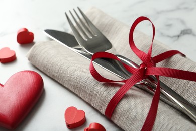 Photo of Romantic place setting for Valentine's day. Cutlery with napkin and red decorative hearts on white marble table, closeup