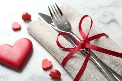 Photo of Romantic place setting for Valentine's day. Cutlery with napkin and red decorative hearts on white marble table, closeup