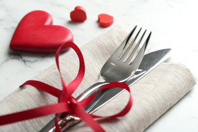 Photo of Romantic place setting for Valentine's day. Cutlery with napkin and red decorative hearts on white marble table, closeup