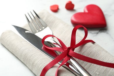 Photo of Romantic place setting for Valentine's day. Cutlery with napkin and red decorative hearts on white marble table, closeup