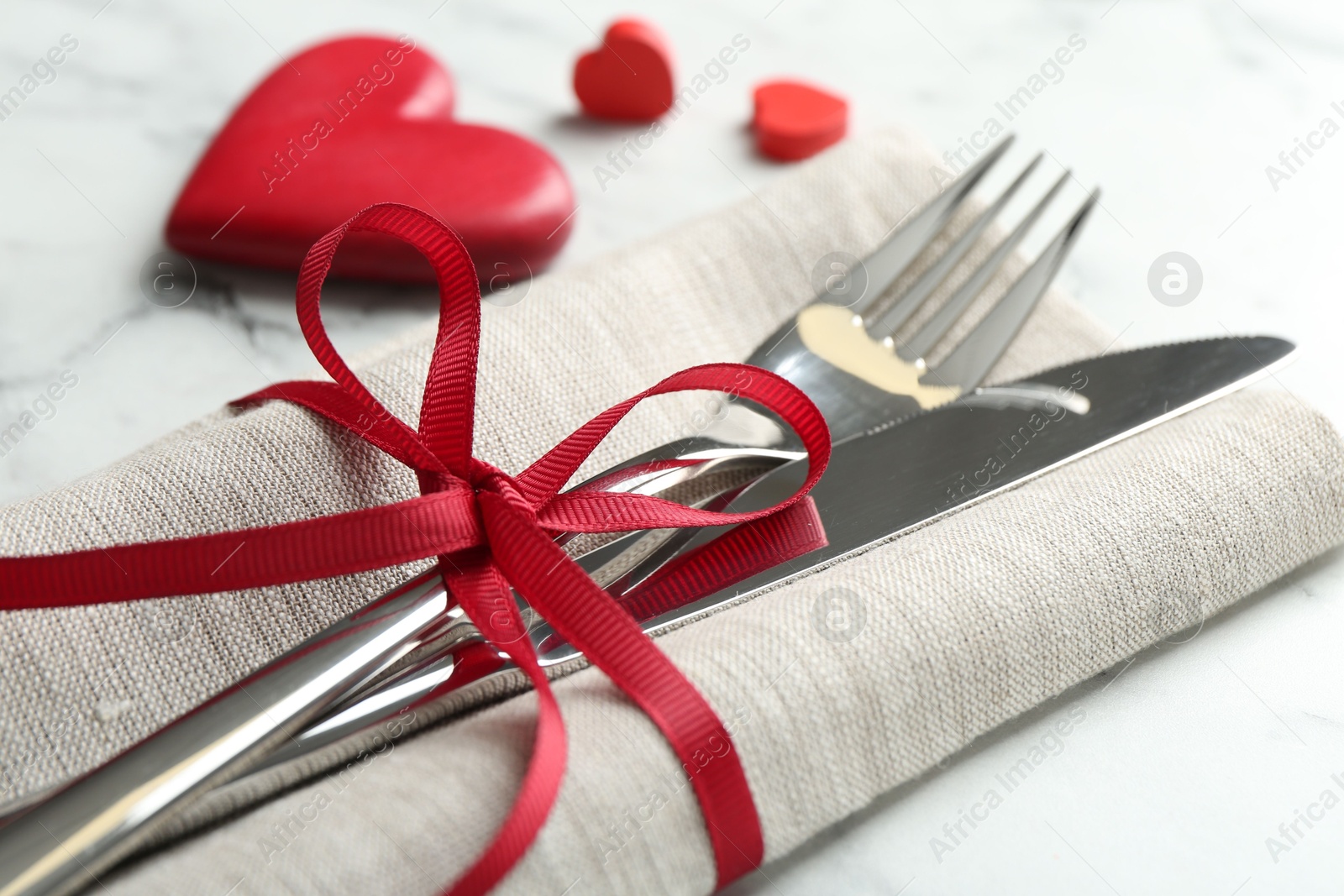 Photo of Romantic place setting for Valentine's day. Cutlery with napkin and red decorative hearts on white marble table, closeup