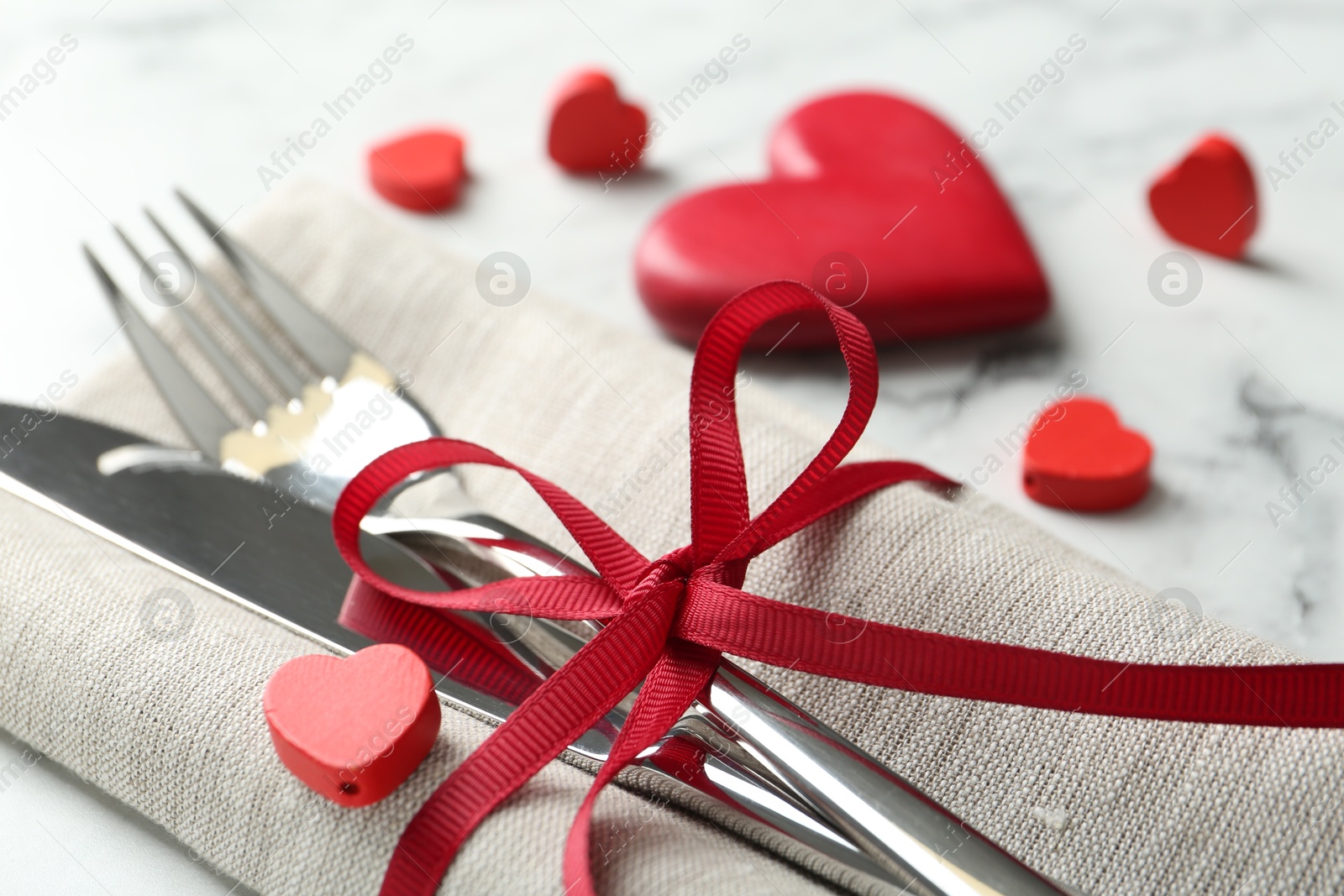 Photo of Romantic place setting for Valentine's day. Cutlery with napkin and red decorative hearts on white marble table, closeup