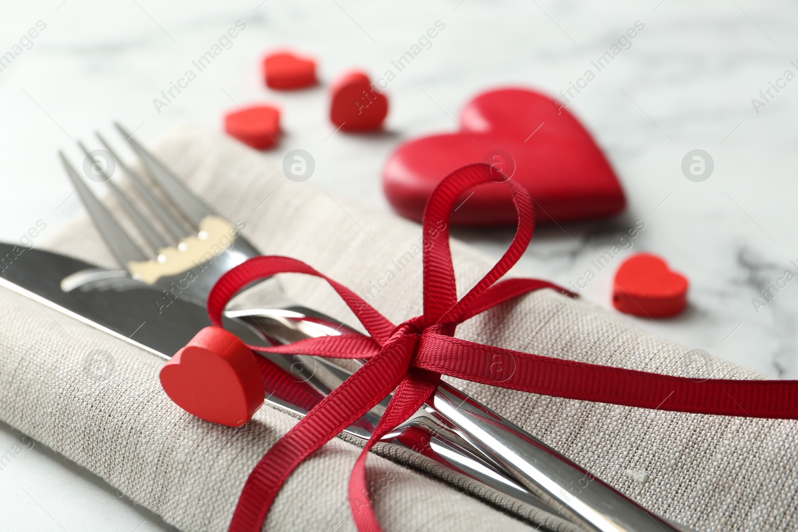 Photo of Romantic place setting for Valentine's day. Cutlery with napkin and red decorative hearts on white marble table, closeup