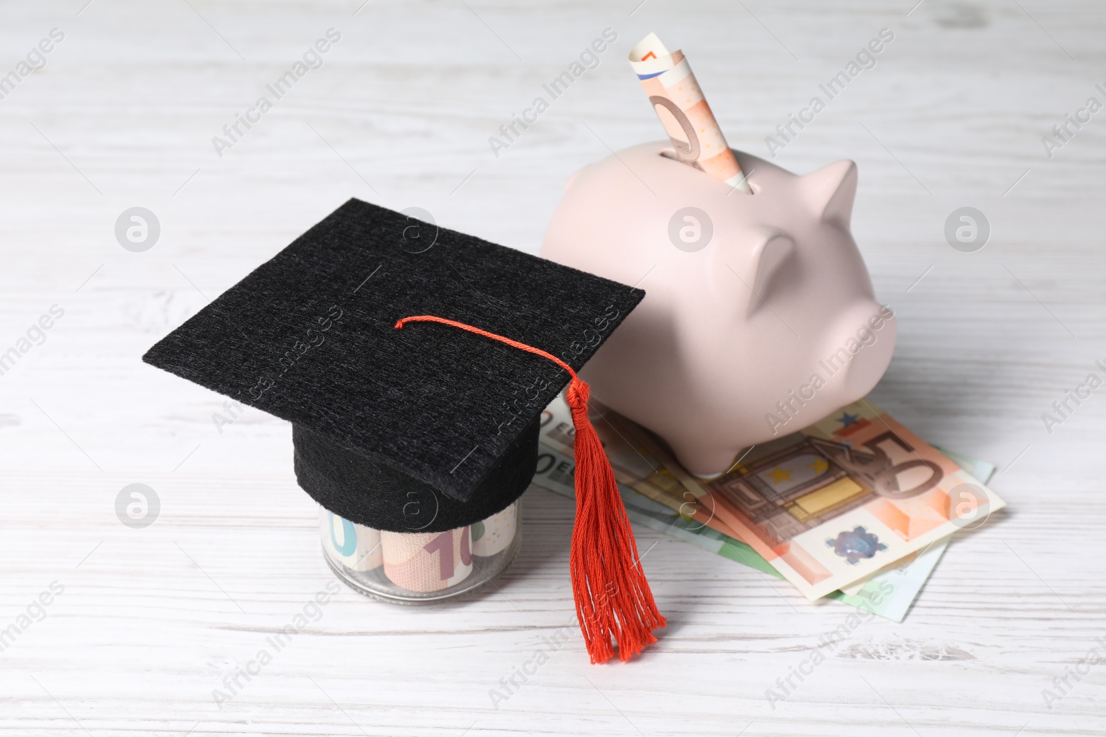 Photo of Graduate hat, euro banknotes and piggy bank on light wooden table. Tuition payment