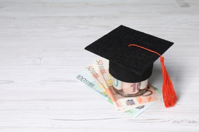 Photo of Tuition payment. Graduate hat and euro banknotes on light wooden table. Space for text