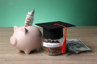 Photo of Graduate hat, dollar banknotes, piggy bank and coins in glass jar with word Education on wooden table. Tuition payment